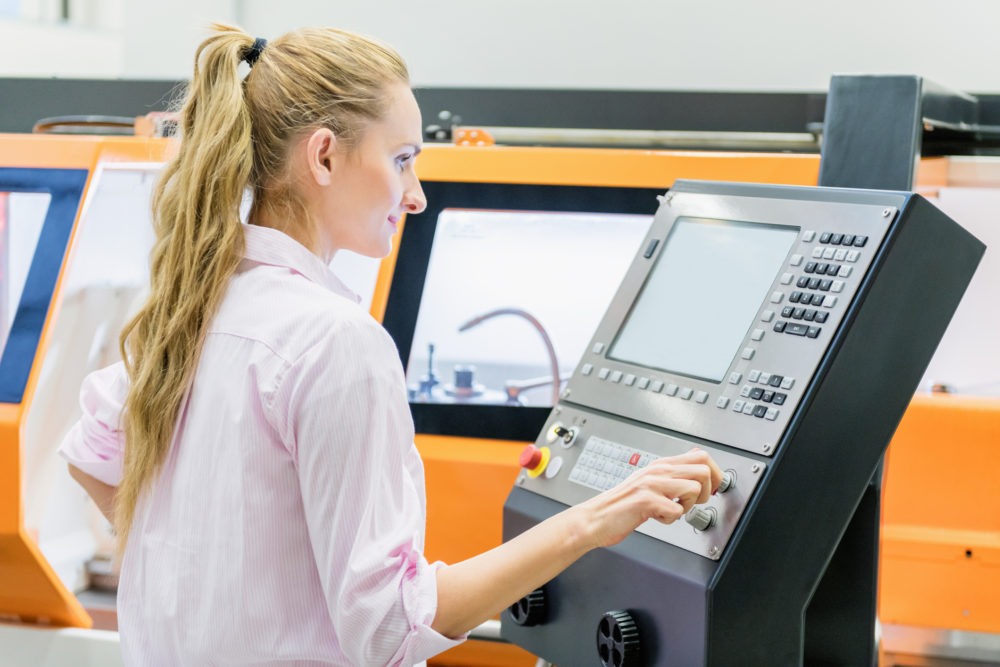 Horizontal color image of woman programming a cnc machine in factory.