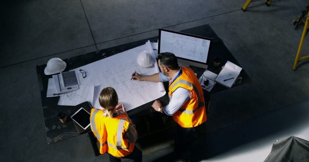 High angle shot of two engineers going over a blueprint together in an industrial place of work