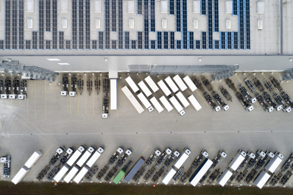 Aerial view of semi trucks during unloading and a large storehouse with solar panels on the rooftop.